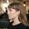 Woman in salon chair with blunt fringe showing slight root crease before styling in warm morning light