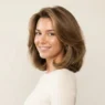 Woman with full bouncy collarbone-length lob blowout showing volume and glossy movement against cream backdrop