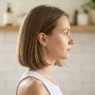 Woman with a chin-length bob seen in side profile in a bright home bathroom before any styling technique is applied