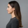 Woman with long chocolate brown hair shown in side profile against grey backdrop with bright even studio lighting