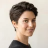 Woman with classic tapered pixie cut against warm white backdrop showing clean taper at sides and volume on top