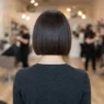 Back view of woman in salon with completed short bob showing sharp horizontal perimeter line across nape, soft even lighting