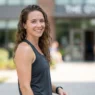 Woman outside gym with slightly damp hair pushed back from face in bright open daylight