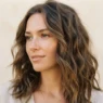 Woman with softly tousled lived-in waves against a warm plain backdrop, three quarter view showing effortless texture from crown to collarbone