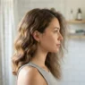 Woman in bathroom with one side of hair styled in waves and the other side still unstyled, showing the sectioning contrast