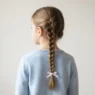 Young girl with a neat French braid running down her back secured with a pastel ribbon in soft indoor light