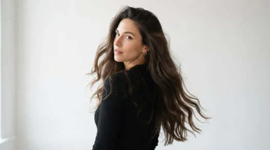 Woman with long dark open hair looking back over shoulder showing full volume and movement against white backdrop