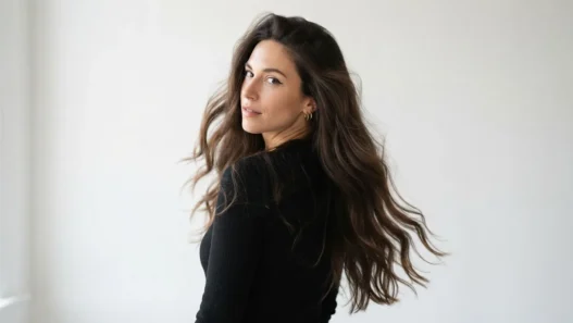 Woman with long dark open hair looking back over shoulder showing full volume and movement against white backdrop