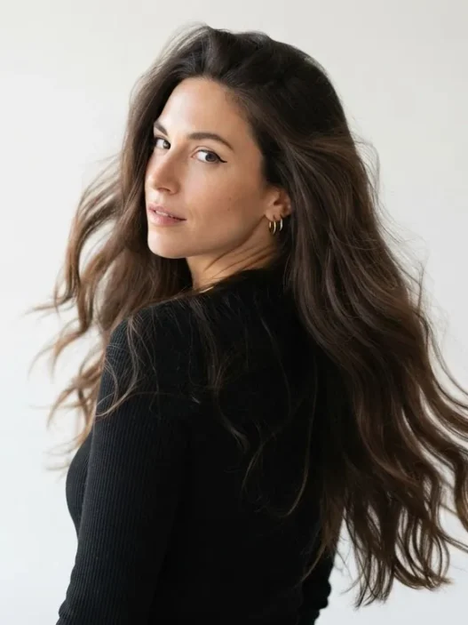 Woman with long dark open hair looking back over shoulder showing full volume and movement against white backdrop