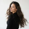 Woman with long dark open hair looking back over shoulder showing full volume and movement against white backdrop