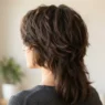 Back three quarter view of woman with thick hair in short chin-grazing layers with longer underlayers visible in soft natural light