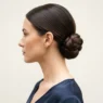 Woman wearing a smooth low nape chignon in side profile against a pale cream backdrop with soft even lighting
