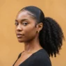 Woman with tightly coiled 4C natural hair in a high sleek ponytail with laid edges against a warm amber backdrop