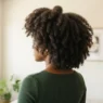 Back three quarter view of woman with thick natural 4C coily hair in bright room showing full crown width
