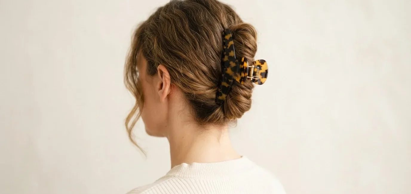 Woman wearing tortoiseshell claw clip in low twisted chignon updo, soft indoor light against warm white wall