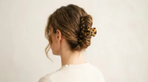 Woman wearing tortoiseshell claw clip in low twisted chignon updo, soft indoor light against warm white wall