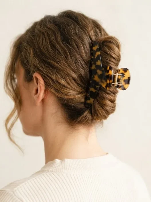 Woman wearing tortoiseshell claw clip in low twisted chignon updo, soft indoor light against warm white wall