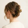 Woman wearing tortoiseshell claw clip in low twisted chignon updo, soft indoor light against warm white wall